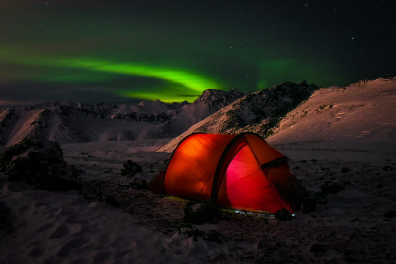 A tent in a snowy mountain with Aurora Borealis in the sky