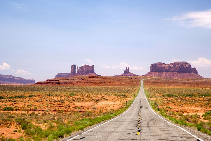 A straight, empty road stretches through a vast desert under a clear blue sky