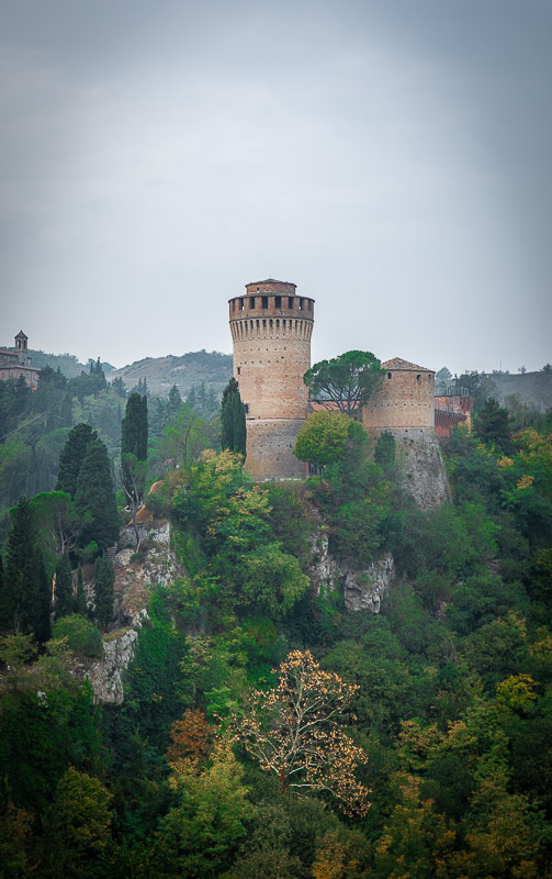 Brisighella's castle stands atop a lush hill, embraced by a beautiful forest