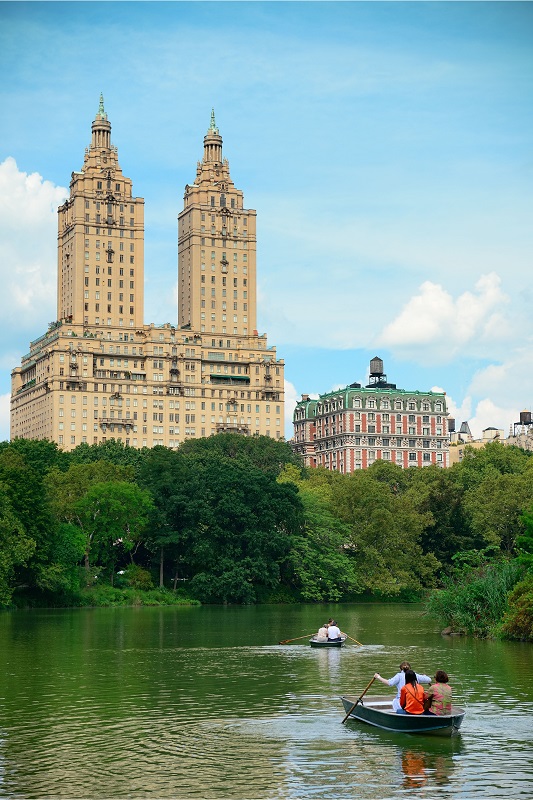 Central Park in Manhattan: Tourists enjoying boat rides on the tranquil lake amid lush greenery and iconic skyscrapers in the background.