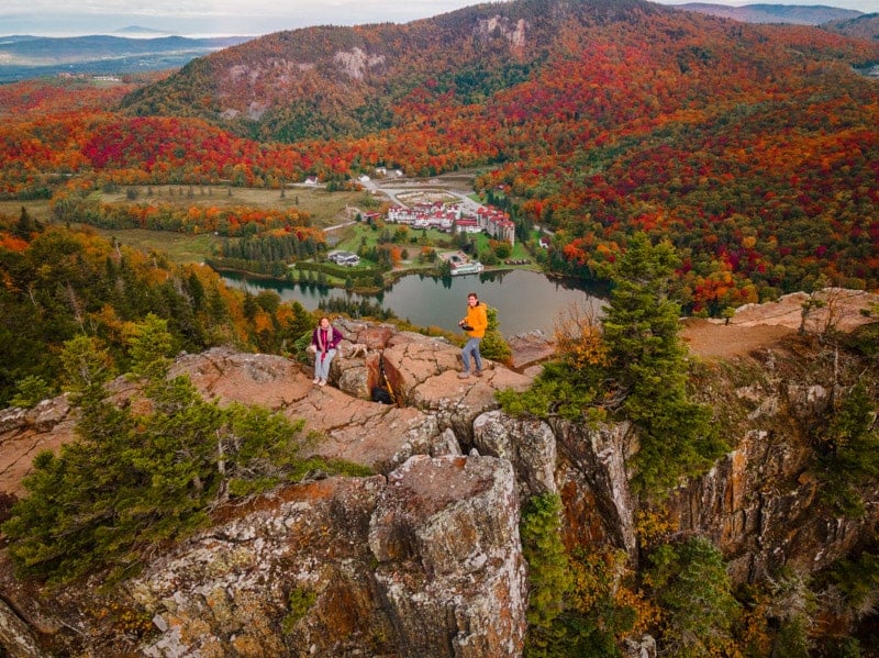 Two people enjoying a breathtaking view of a lake and mountains from a cliff in New England