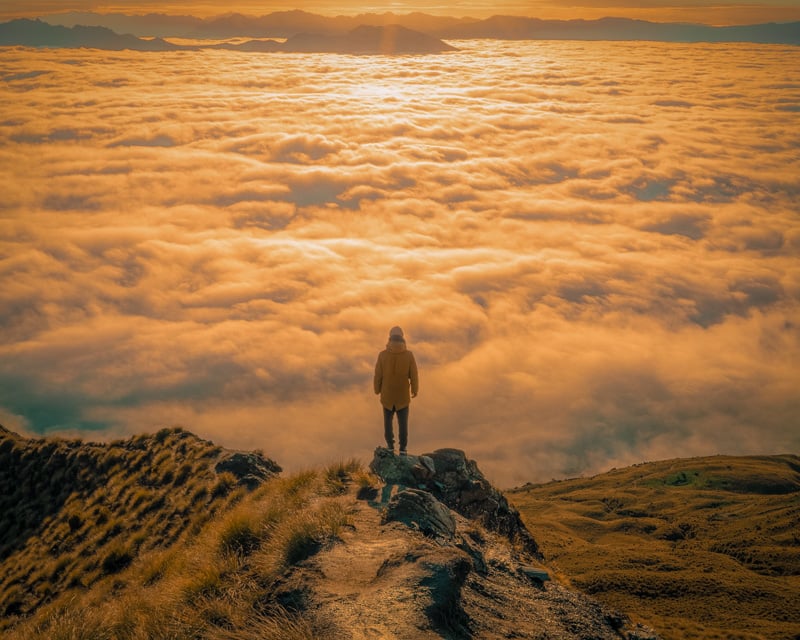 A man on a mountain peak gazes at the clouds, captivated by the breathtaking view