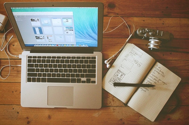 A laptop, notebook and camera on a wooden table