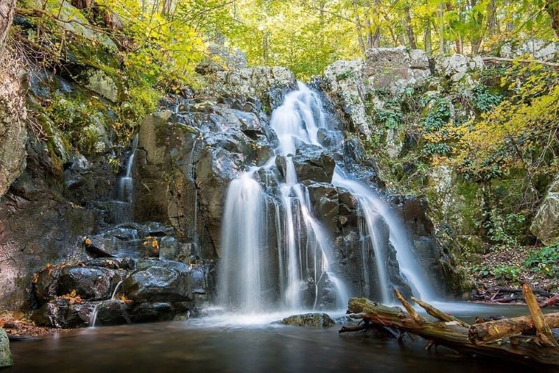 A picturesque view of Overall Run Falls, a stunning waterfall framed by rocks and foliage, inviting contemplation