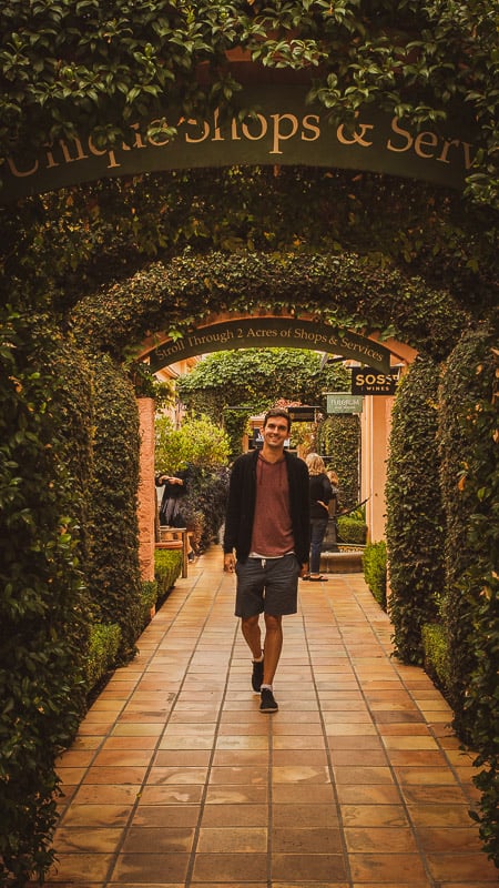 Jon strolling through a garden's archway, surrounded by lush greenery and vibrant flowers