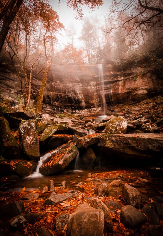 A serene waterfall surrounded by colorful autumn leaves in a picturesque woodland setting