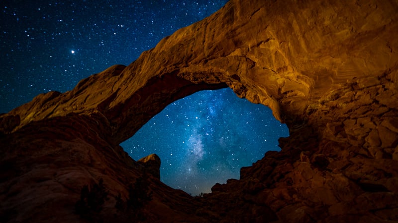 The Milky Way shining brightly over a rock arch in the desert at night
