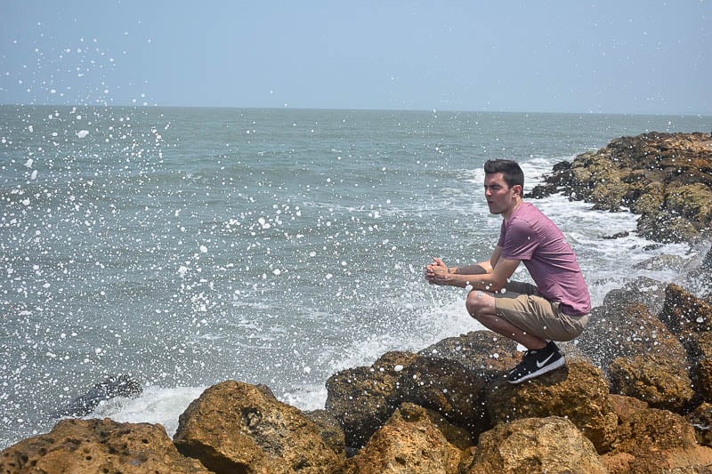 Jon sitting on rocks in the ocean, while the water splashes on him