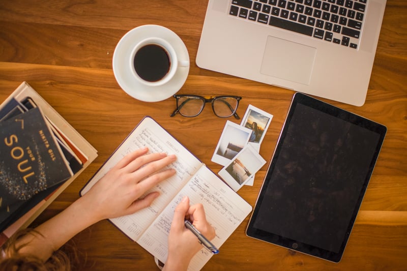 Woman multitasking with laptop, notebook, and coffee on table