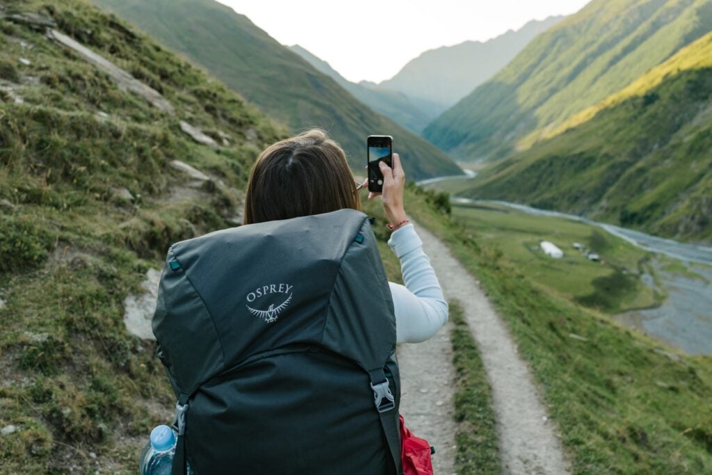 Woman hiking in the mountains taking a picture with her phone.