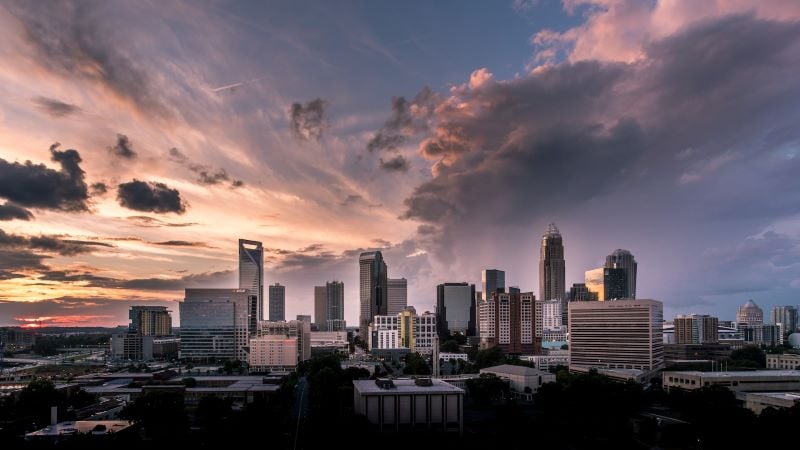 Silhouettes of buildings in Charlotte against a colorful sunset sky filled with clouds